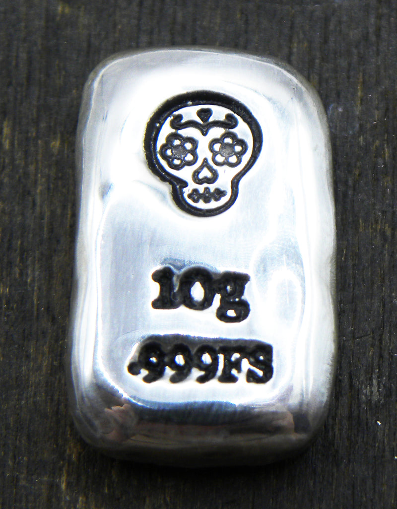 Close-up of a 10-gram 999 fine silver rectangular bar with a polished, reflective surface. The Sugar Skull stamp is stamped on the top half of the bar and 10g 999FS on the bottom half. The bar is positioned vertically.