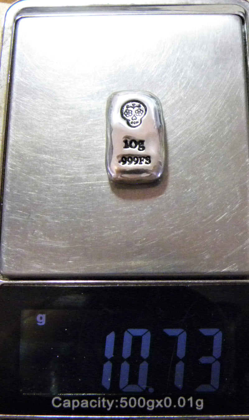 Distant view of a shiny 10g silver (999FS) rectangular bar, featuring a stamped Sugar Skull and 10g 999FS stamped below. The bar is placed  vertically on a digital weight scale.